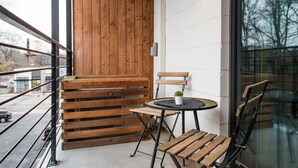 A balcony with wooden benches and a small table with chairs, a potted plant, and a view of the street. - La Penelope – Walk to Ponce City Market + Rooftop (Atlanta)