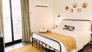 A bedroom with a bed, a bedside table, a lamp, a window with curtains, and wall art. - La Penelope – Walk to Ponce City Market + Rooftop (Atlanta)