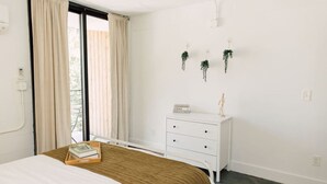 Un dormitorio con cama, cómoda, ventana con cortinas y una planta pequeña en la pared.