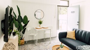 A compact living space with a black sofa, white chairs, a small table with a plant, and a TV mounted on the wall. - The Camille – Skyline Views + Rooftop in Atlanta (Atlanta)