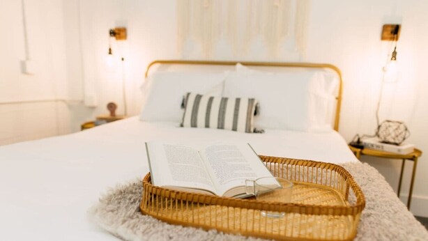 A neatly made bed with a book and a glass on a woven tray, a fluffy rug, and a bedside table with a lamp. - The Camille – Skyline Views + Rooftop in Atlanta (Atlanta)