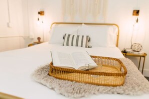 A neatly made bed with a book and a glass on a woven tray, a fluffy rug, and a bedside table with a lamp.