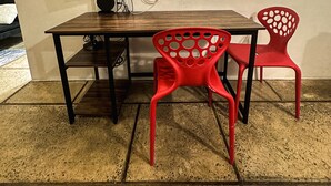 Ein Zimmer mit einem Holztisch, einem roten Stuhl, einem schwarzen Fernseher und einer dekorativen Leuchte.
