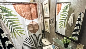 Ein Badezimmer mit Toilette, Waschbecken und Duschvorhang mit Blättermotiv.