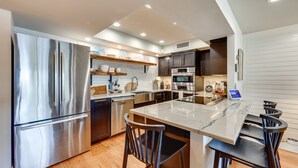 A modern kitchen with stainless steel appliances, a marble island, and dark cabinetry. - Amazing sunrises & beach views from private balcony & steps from the sand!! (Jacksonville Beach)