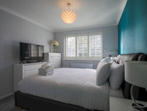 Une chambre à coucher moderne, équipée d’un lit, d’une télévision, d’une commode et d’une fenêtre avec des stores.