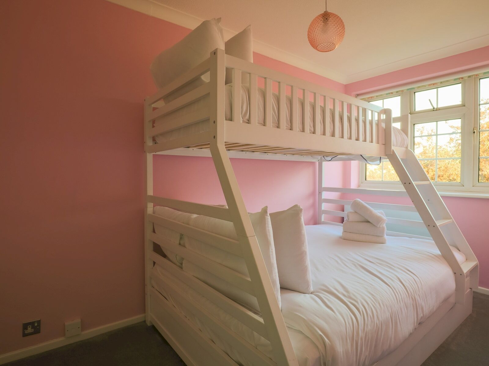 A bunk bed room with pink walls and a window.