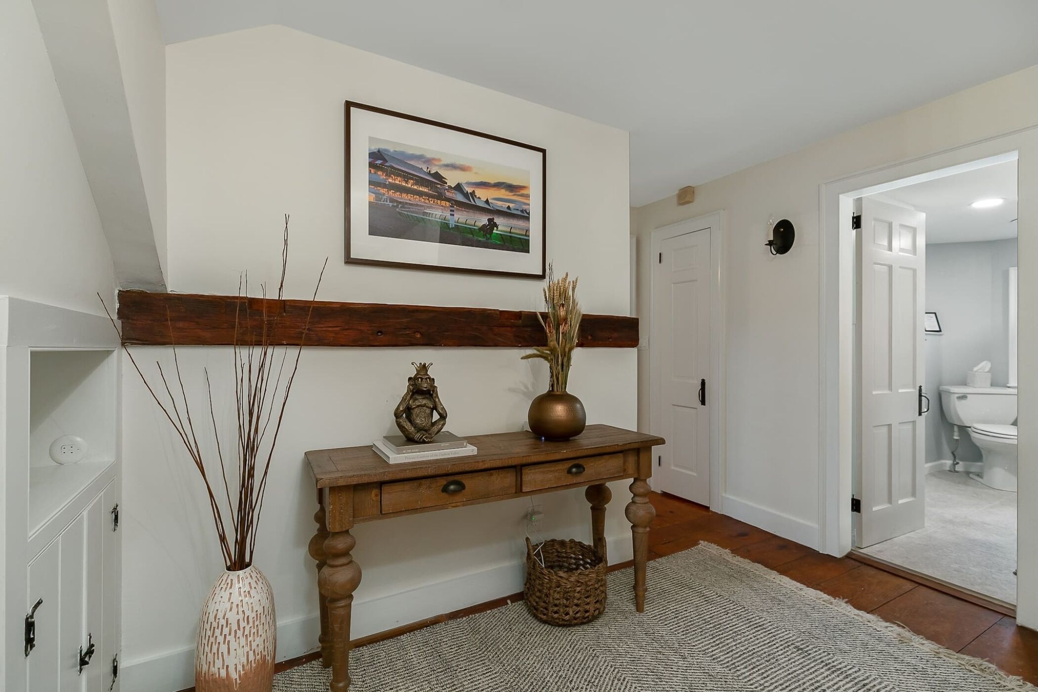 A hallway with a wooden console table, a framed picture on the wall, a vase with dried plants, and a basket.