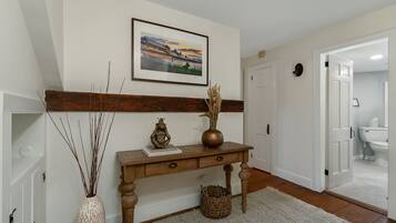 A hallway with a wooden console table, a framed picture on the wall, a vase with dried plants, and a basket.