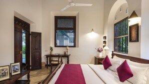 Een hotelkamer met een bed, een bureau, een stoel, een plafondventilator, een raam met tralies en een deur.