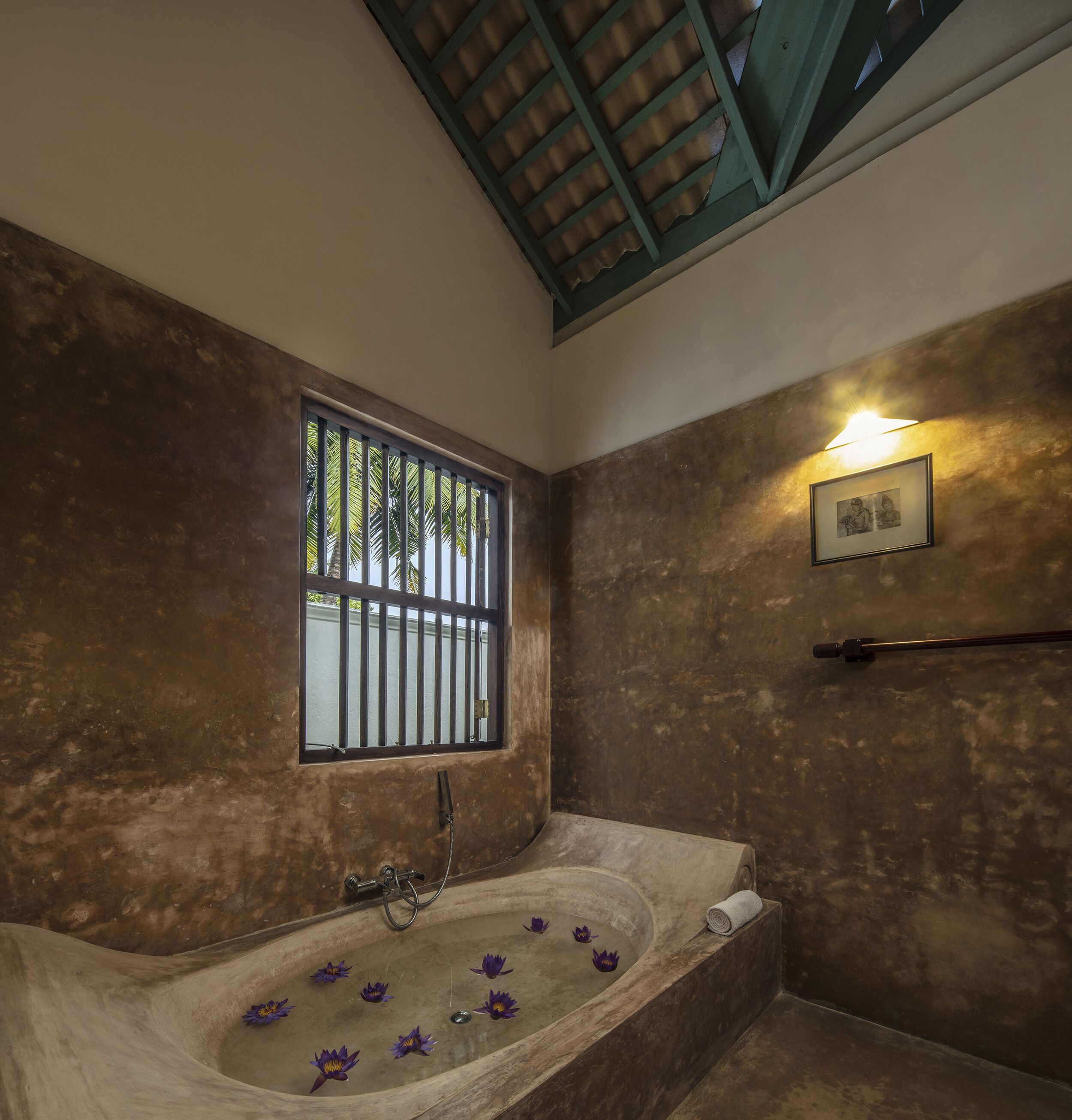 Une salle de bain avec une baignoire, une fenêtre avec des barreaux, un porte-serviettes et un luminaire fixé au mur.
