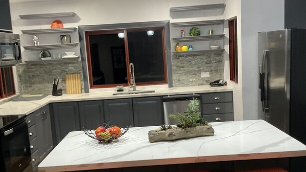Une cuisine moderne dotée d’un îlot central, de tabourets de bar, d’un réfrigérateur et de luminaires suspendus.