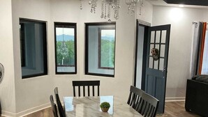 Un espace repas comprenant une table en marbre, des chaises noires, un lustre et de grandes fenêtres donnant sur un paysage verdoyant.