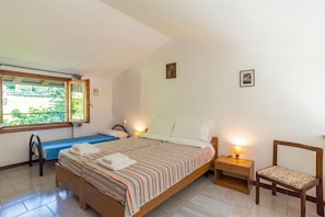 Een slaapkamer met een bed, nachtkastjes, een stoel, een raam en een aan de muur hangend schilderij.