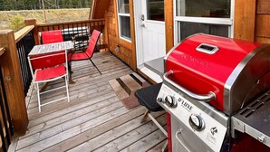 Eine Holzterrasse mit Grill und roten Stühlen, mit Blick auf eine bewaldete Landschaft.