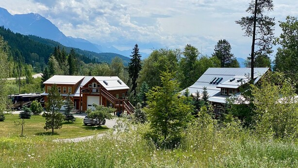 Eine Lodge mit einer großen Garage, einer überdachten Terrasse und einem malerischen Blick auf die Berge.