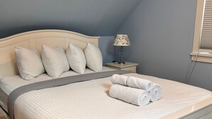 Ein ordentlich bezogenes Bett mit einer gesteppten weißen Decke, einem Kopfteil und einem Nachttisch mit einer Lampe.