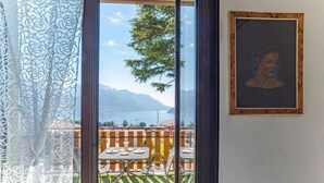 A balcony with a table and chairs, a painting on the wall, and a view of mountains and water. - CO.RI. Appartamenti 2, Menaggio, Italy (Menaggio)