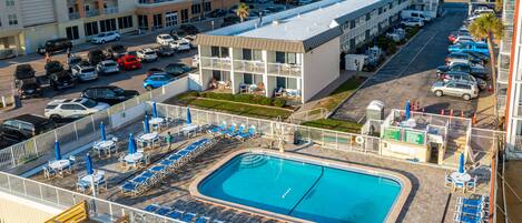 Un hotel con piscina en la azotea, varios estacionamientos y vistas de la ciudad circundante.
