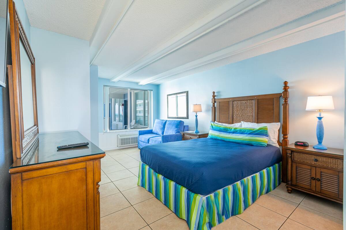 A hotel room with a large bed, a wooden nightstand, a desk, and a chair.