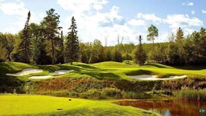Ein Golfplatz mit Sandbunkern, einem Teich und dichter Baumvegetation.