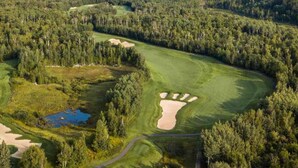 Eine Vogelperspektive eines Golfplatzes mit Sandbunkern, einem Teich und dichter umliegender Waldlandschaft.
