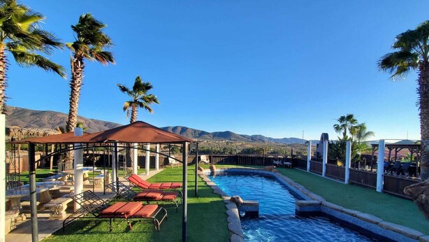 A pool area with a pergola, lounge chairs, and palm trees. - Cozy Cabin with Terrace and Panoramic View- Access to Pool (Ejido El Porvenir (Guadalupe))