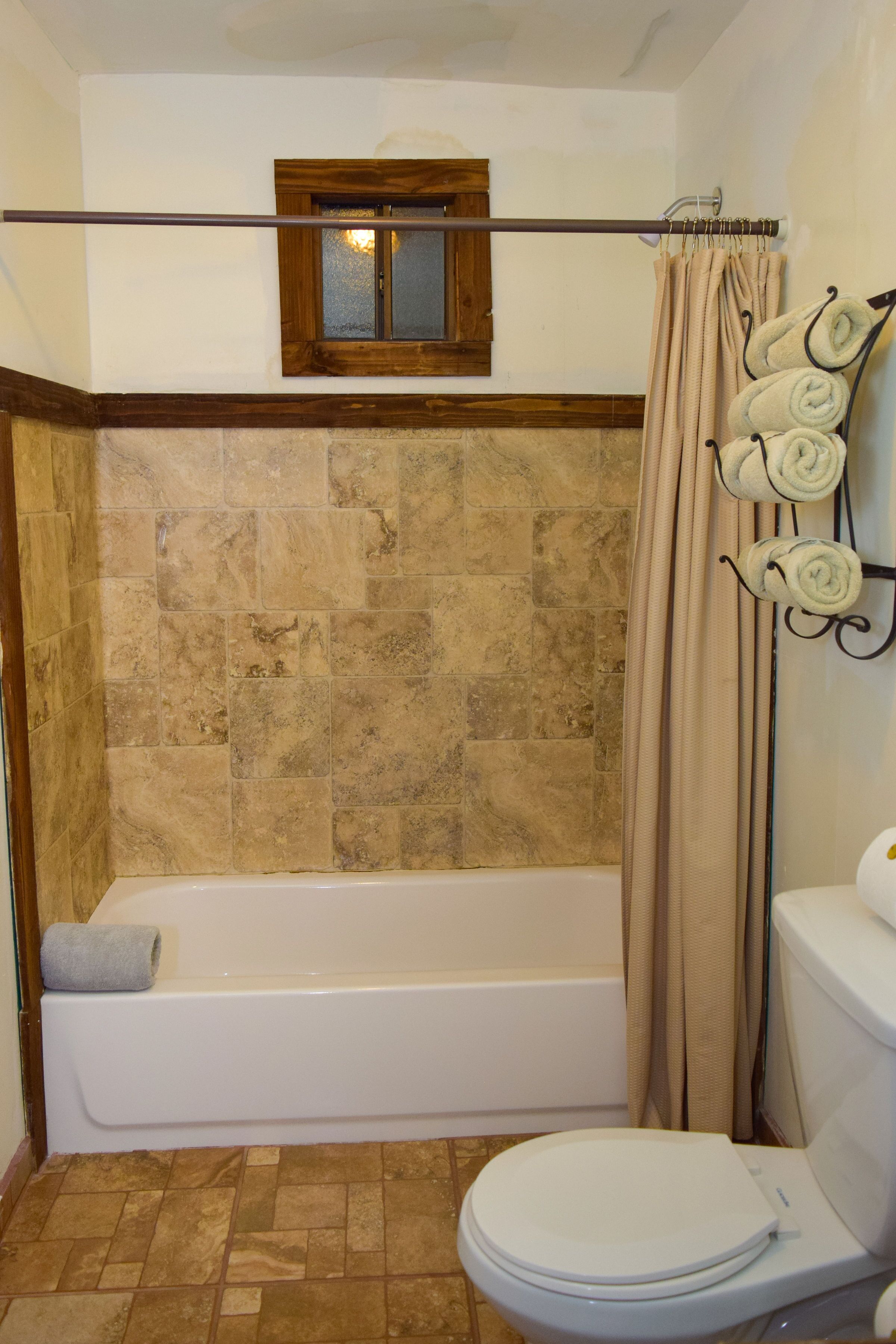 Ein Badezimmer mit Badewanne, Toilette und einem Fenster über der Wanne.