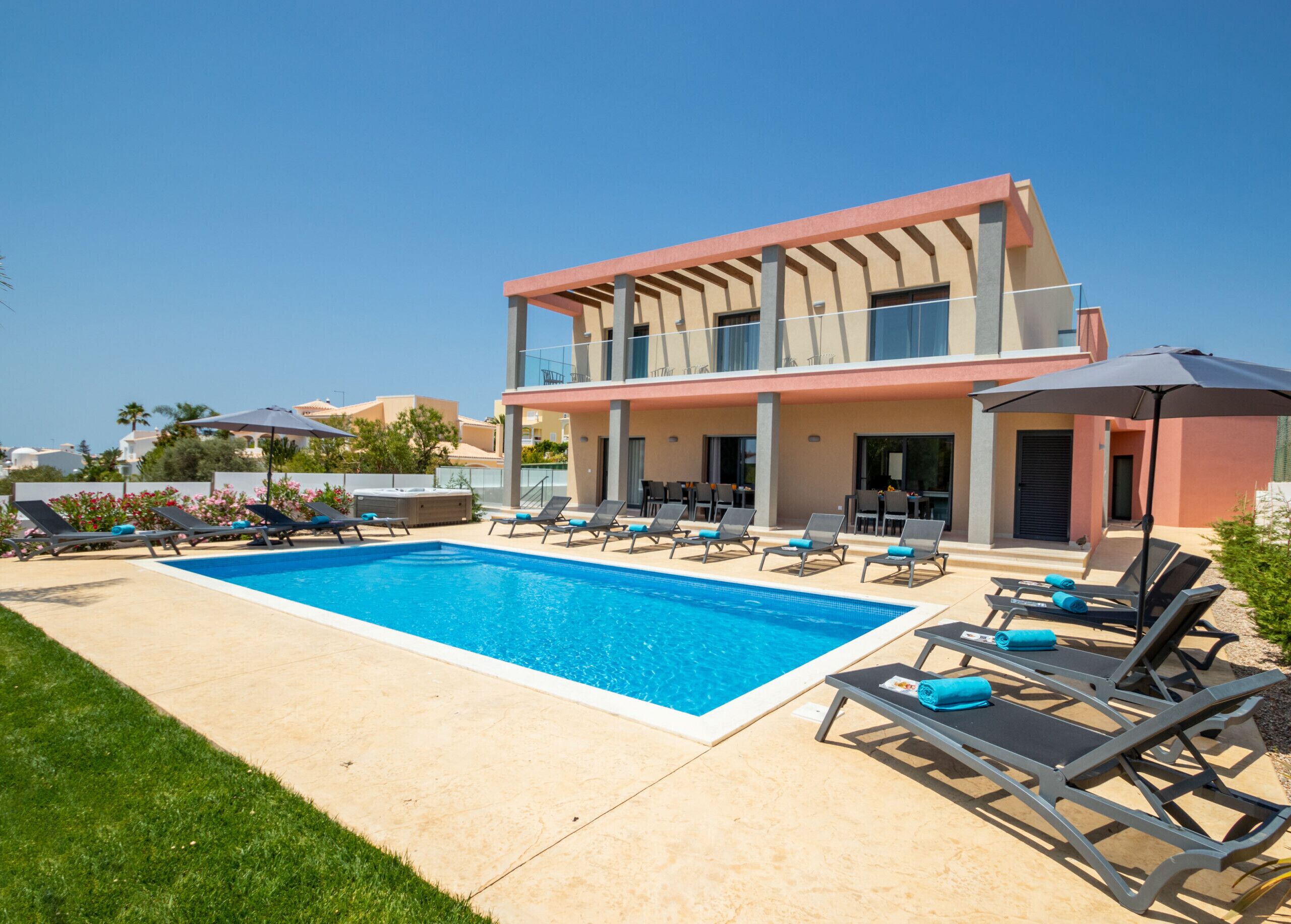 A modern hotel with a swimming pool, lounge chairs, and a two-story building.