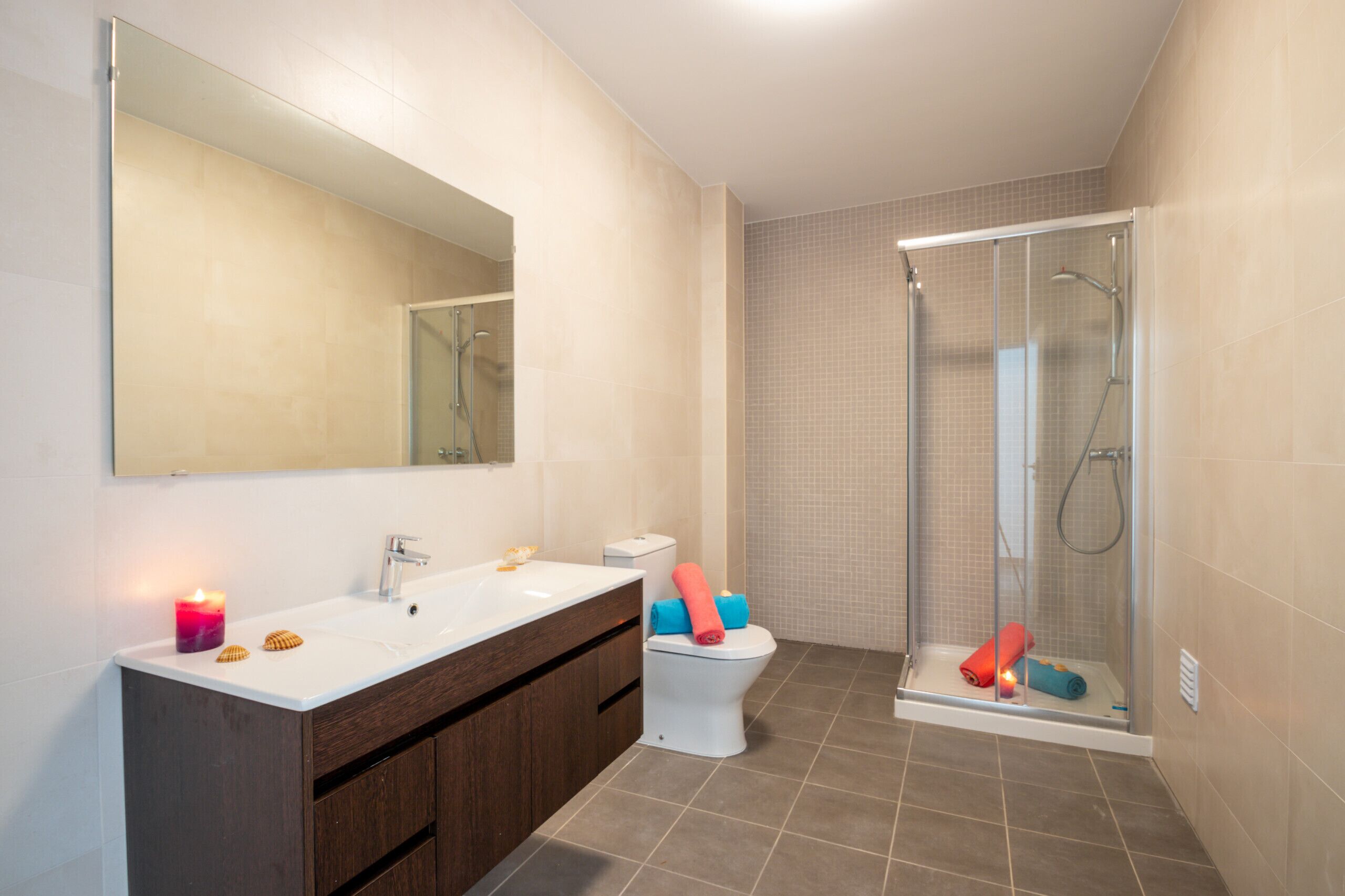 Un baño moderno con un espejo grande, dos lavamanos, un inodoro y una cabina de ducha de vidrio.