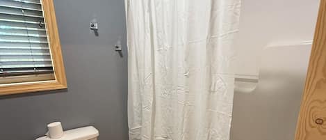Un baño con inodoro, ducha y ventana con persianas.