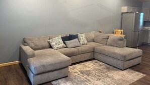 A living room with a sectional sofa, a rug, and a kitchen area in the background. - Baja Motel (Oakland)