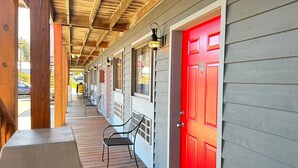 A covered porch with wooden beams, metal chairs, and a bright red door. - Baja Motel (Oakland)