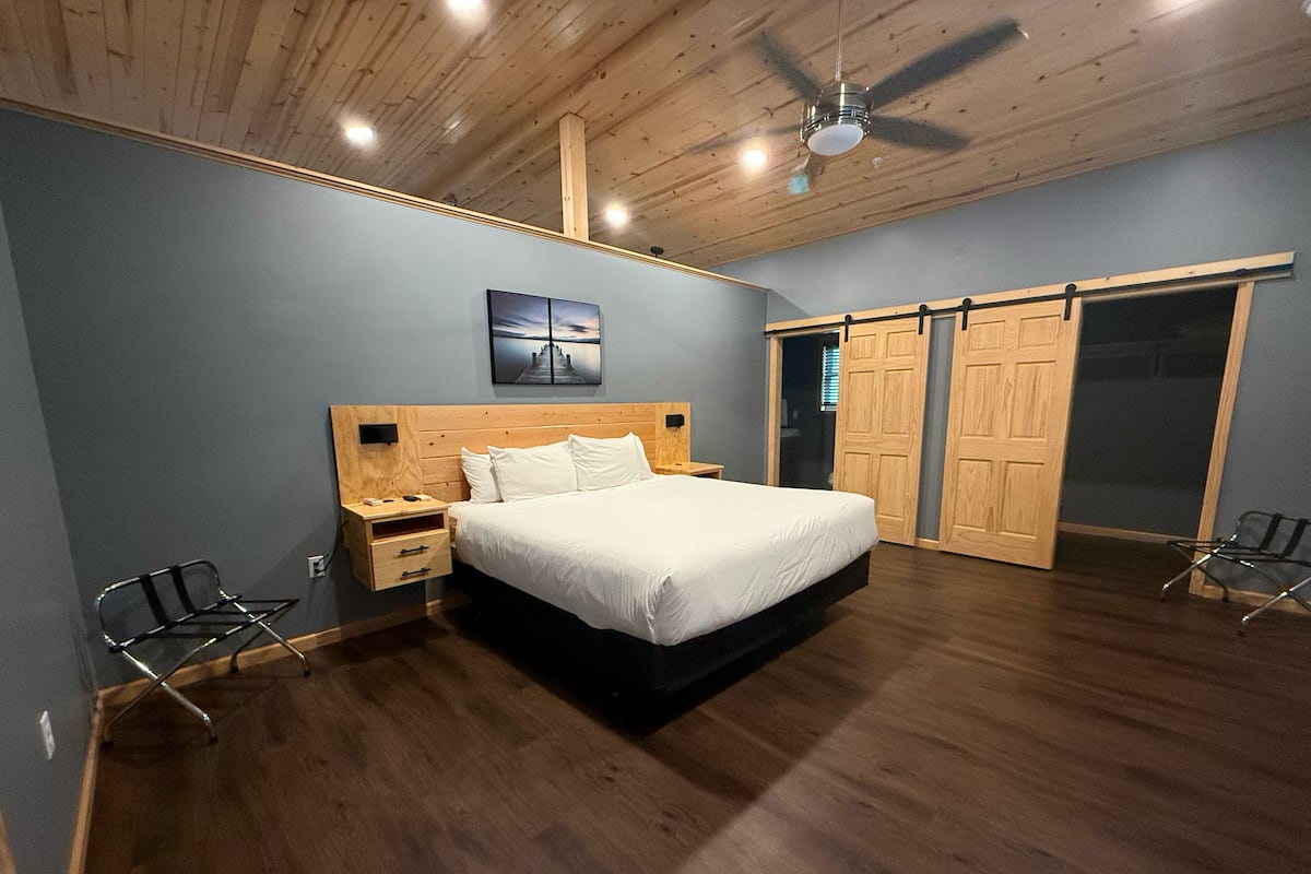 A bedroom with a wooden ceiling, a bed, a nightstand, a chair, and a wardrobe.