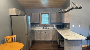 A kitchen with wooden cabinets, a refrigerator, a microwave, a sink, and a window with blinds. - Baja Motel (Oakland)