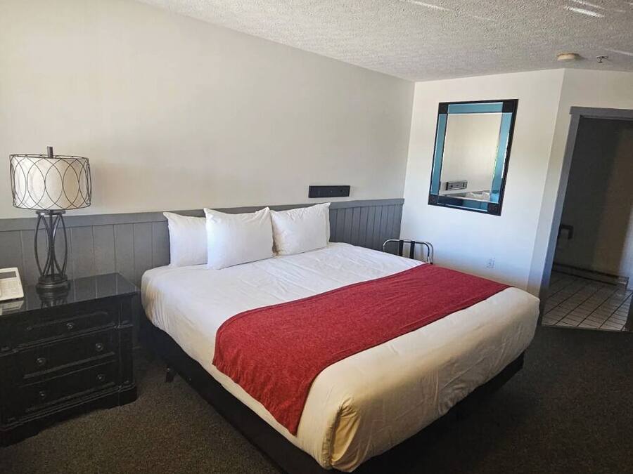 A hotel room with a bed, a nightstand, a lamp, and a mirror on the wall.