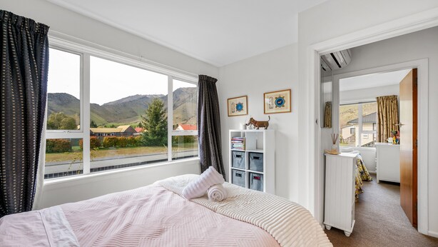 A bedroom with a large window, a bed with a pink blanket, a white dresser, and a view of mountains. - Pops Place - Omarama Holiday Home (Omarama)