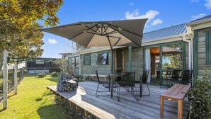 A wooden deck with outdoor furniture, a large umbrella, and a glass door leading to a covered patio.