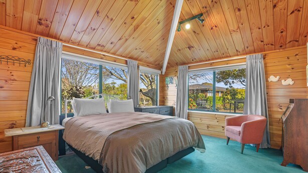 A wooden cabin bedroom with a bed, a chair, a desk, and large windows.