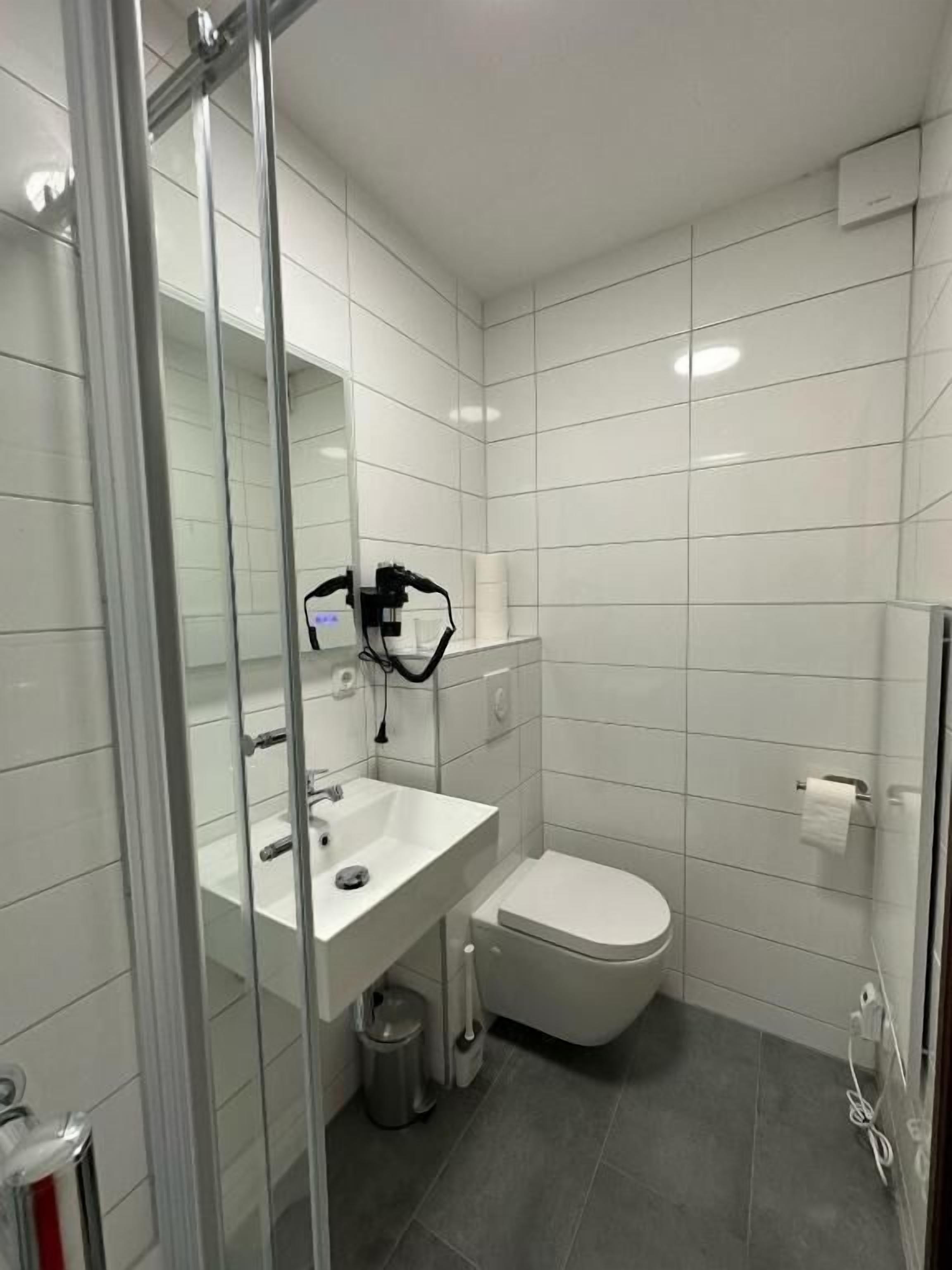 Un baño moderno con cabina de ducha de vidrio, un lavabo blanco y un inodoro.