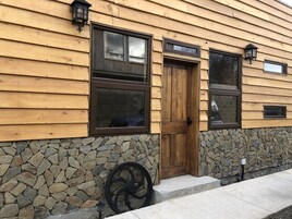 Un edificio de madera con zócalo de piedra, puerta de madera y varias ventanas.