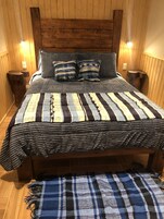 Una cama de madera con un edredón a rayas y dos almohadas, flanqueada por mesitas de noche de madera.