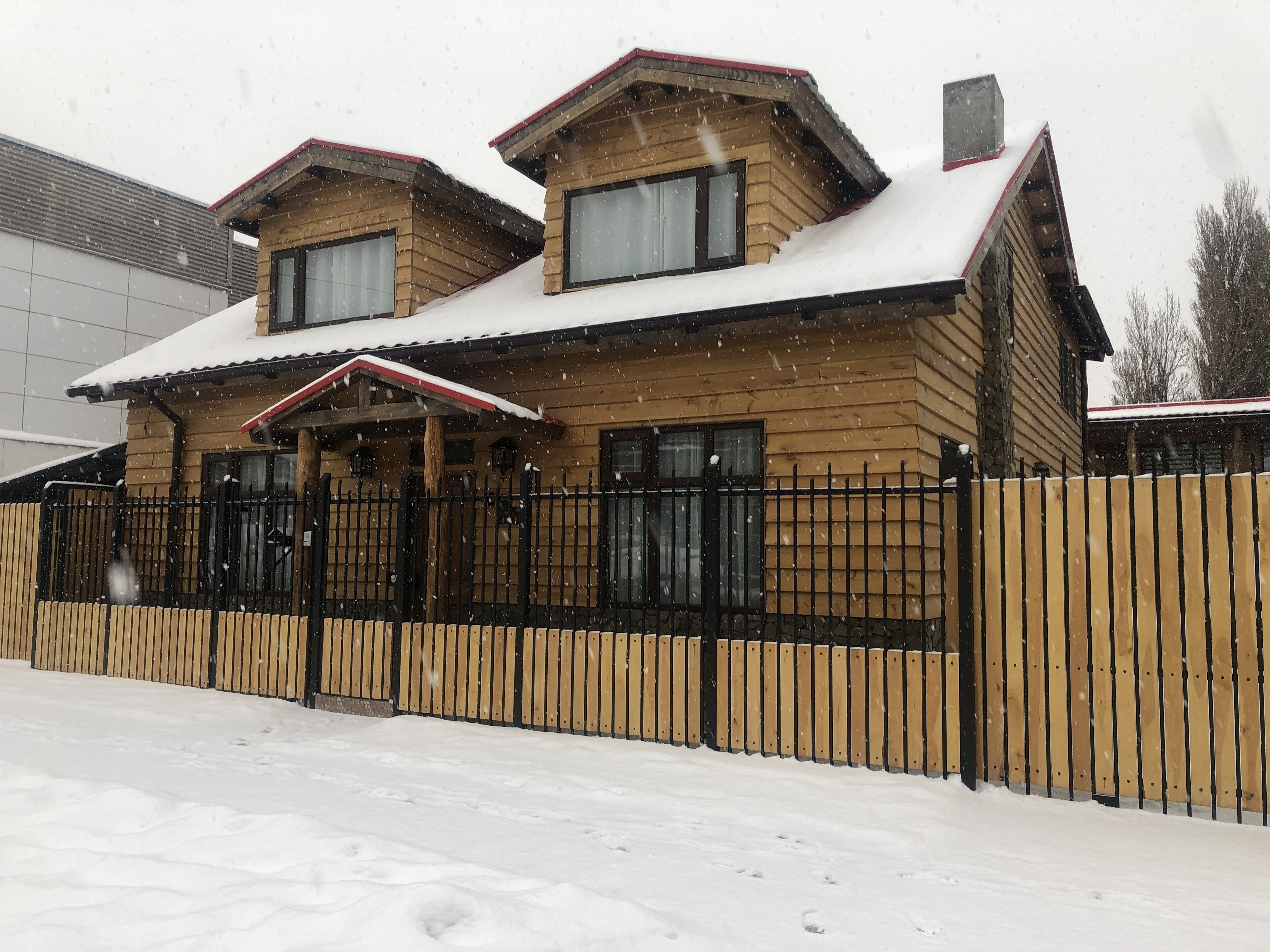 Una casa de fusta de dos pisos amb un sostre cobert de neu i una tanca de metall negra.
