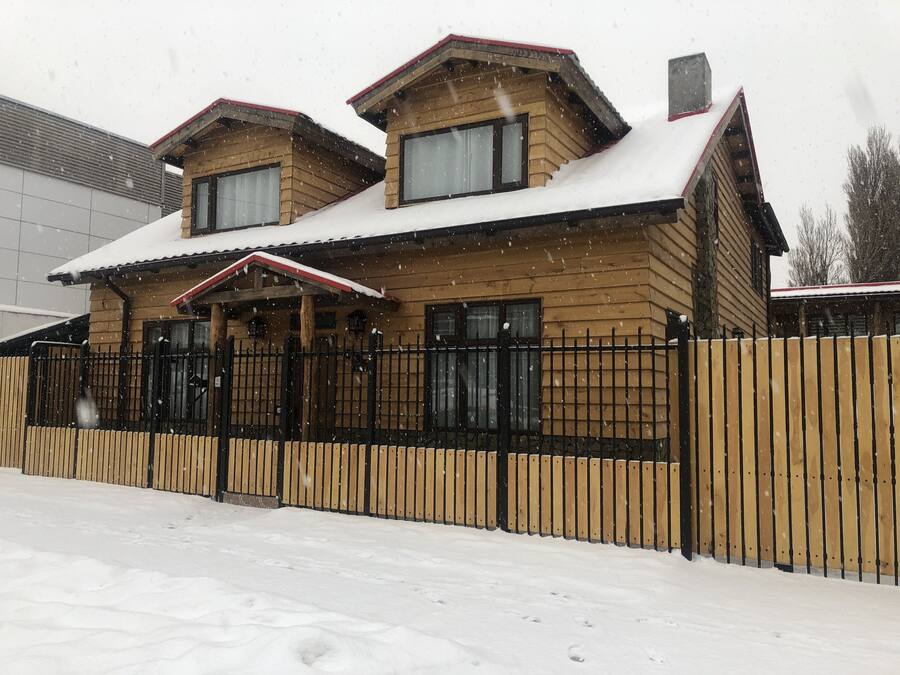 Una casa de fusta de dos pisos amb un sostre cobert de neu i una tanca de metall negra.