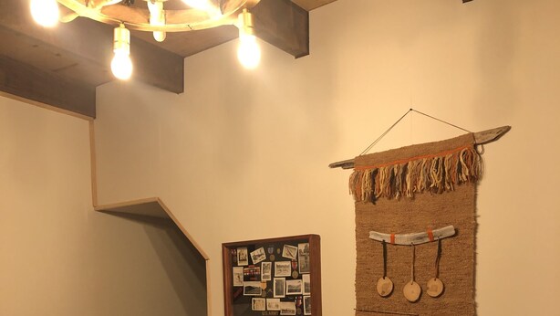 A room with a wooden table and a black chair, a wall-mounted photo collage labeled "US Army," and a decorative wall hanging with tassels and circular ornaments. - Magellanicus Rustic Suites (Punta Arenas)