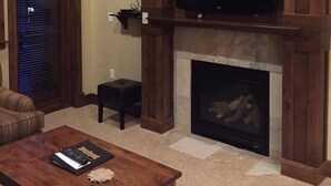 Ein Wohnzimmer mit Kamin, einem darüber montierten Fernseher, einem Sofa und einem Couchtisch.