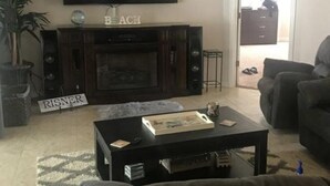 Una sala de estar con una televisión de pantalla plana sobre una chimenea, una mesa de centro, un sofá y una planta en maceta.