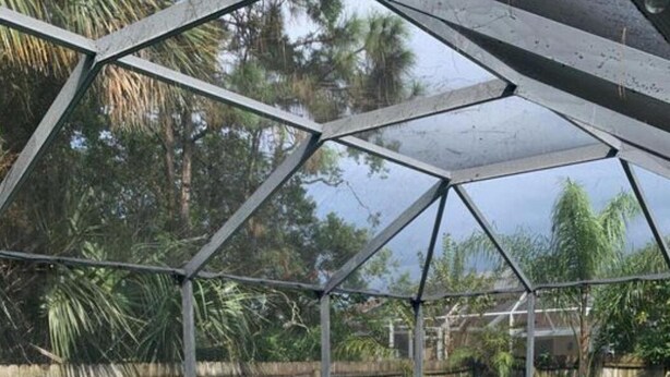 Una piscina con cerramiento de vidrio, rodeada por un patio de ladrillo y sillas azules.