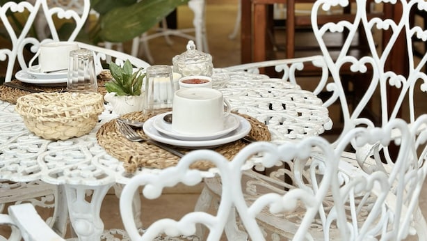 A restaurant with white ornate chairs and tables, a bar area in the background, and hanging plants. - Peixe Crew Rua das Pedras (Búzios)