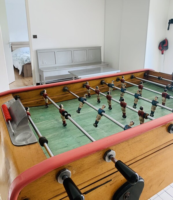 Une table de baby-foot dans une pièce où se trouvent un lit et, au fond, une armoire blanche.